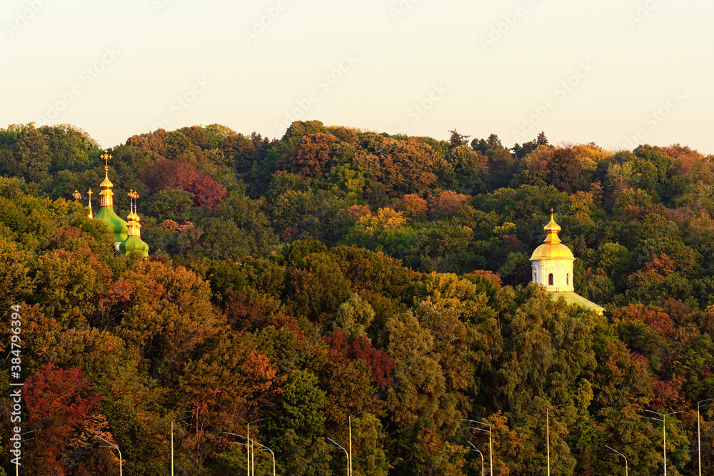Astonishing  morning autumn landscape view of famous Kyiv's hills against blue sky. The domes Saint George's Cathedral and ancient Michael's Cathedral of Vydubychi Monastery over the old trees. Kyiv
