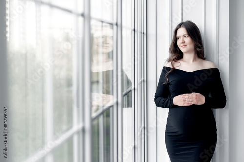 Free Download beautiful young pregnant woman in dark black dress stands near the window - GFXLoad