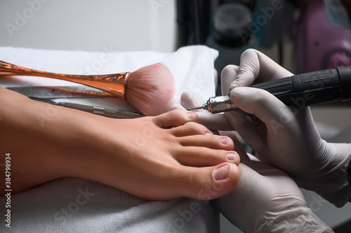 Pedicurist woman removes cuticle from client's toes using electric nail machine, closeup view. Professional hardware pedicure in beauty clinic, side view. Hugiene and care about woman's foot and toes. photo