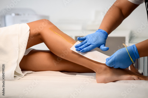 Beautician waxing a woman's leg applying a strip of material over the hot wax to remove the hairs when pulled