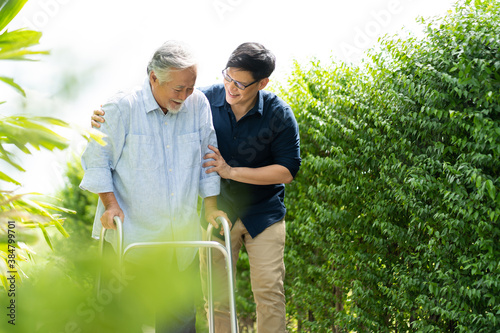 Elderly Asian father and Adult son walking in backyard. Positive Asian man caregiver helping patient photo