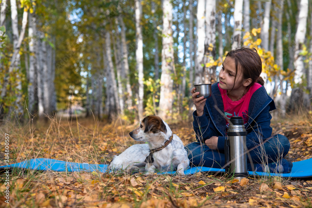 A girl with a mug and a spotted dog on a mat  in the autumn forest saw something and look