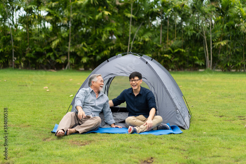 Senior Asian Father With Adult Son Enjoying Camping Holiday. senior mature father and smiling young adult Resting in the tent. Happy family time together.