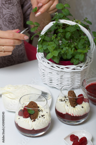 A woman makes a dessert of cream cheese with raspberry jelly. The ingredients are laid out on the table surface. Decorated with cookies  raspberries and mint.