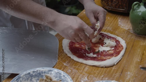 Chef tops Neapolitan pizza with fresh  mozzarella cheese, on wooden table. Slow motion shot. photo