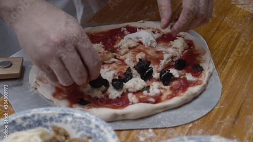 Chef tops Neapolitan pizza with black olives, on wooden table. Slow motion shot. photo