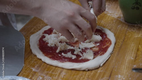 Chef tops Neapolitan pizza with mozzarella cheese, on wooden table. Slow motion shot. photo