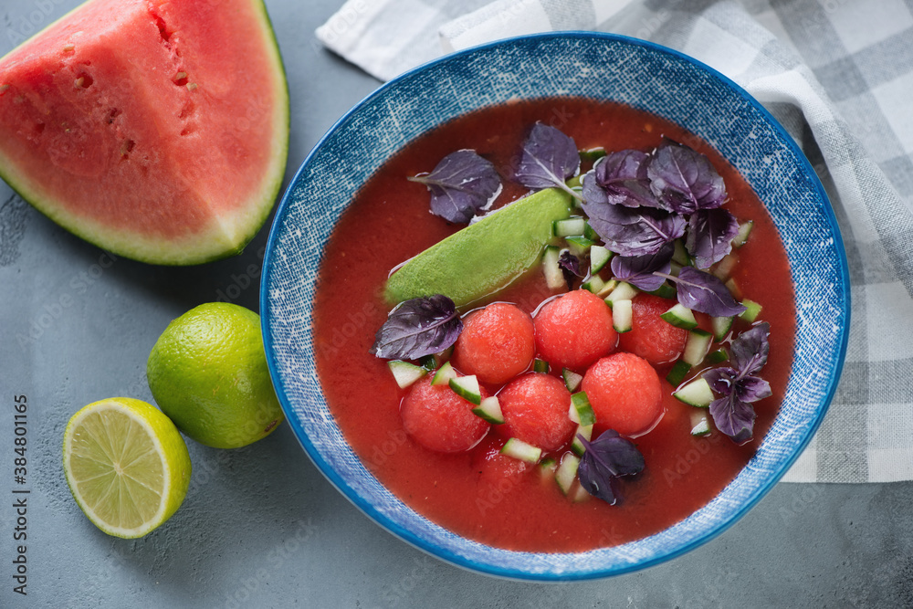 Blue plate with watermelon and tomato gazpacho soup, elevated view on a grey concrete background