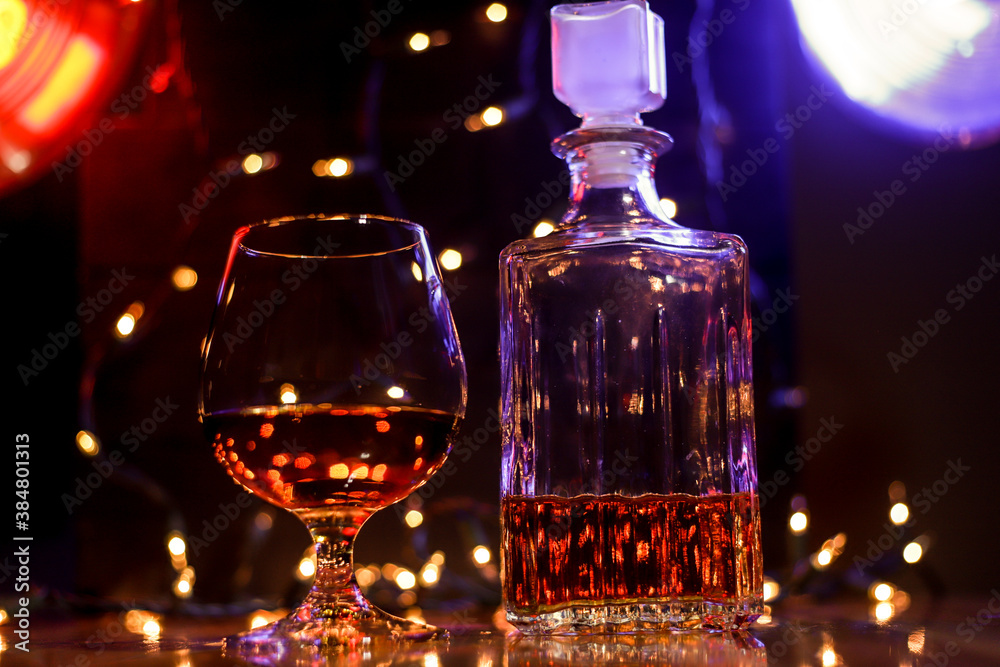 BOTTLE AND GLASS OF BORBON WITH CIGAR AND CHRISTMAS LIGHTS AND COLORED LIGHTS ON WOODEN TABLE AND DARK BACKGROUND BOTTLE AND GLASS OF BORBON WITH CIGAR AND CHRISTMAS LIGHTS AND COLORED LIGHTS ON WOODEN TABLE AND DARK BACKGROUND