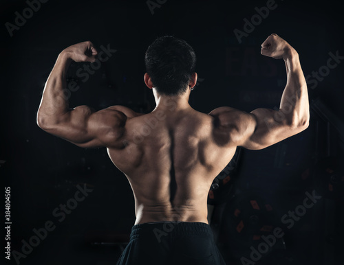 Muscular model young man on dark background. Strong brutal guy showing his biceps triceps, flexing his muscles. back abs. Sport workout bodybuilding healthy lifestyle concept.