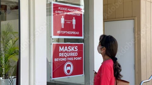 Attractive woman wearing covid mask reads sign instructing social distancing and masks 