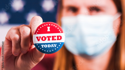 Woman with face mask showing I voted today button with american flag. Extreme close-up