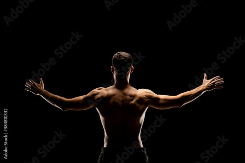 Rear view of muscular man with outstretched arms isolated on black background.