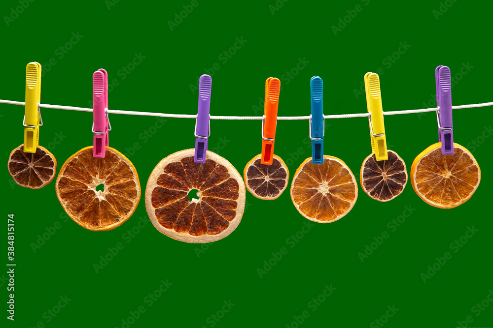 dried pieces of different citrus fruits hang on colored clothespins on a green background dried pieces of different citrus fruits hang on colored clothespins on a green background