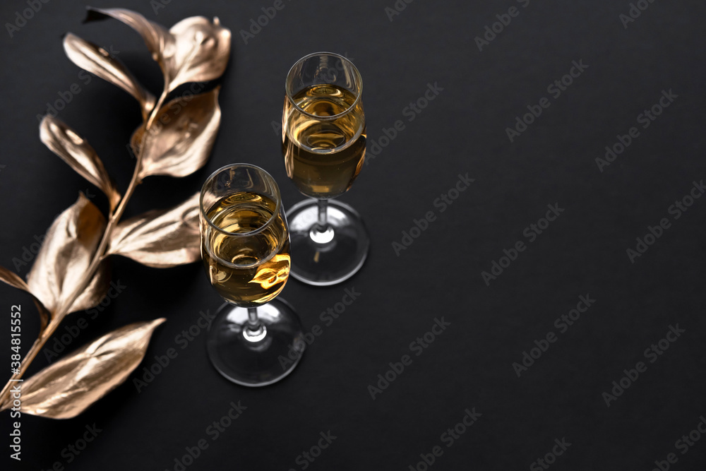 Two glasses of champagne over black background and golden Christmas decoration. Holiday decorations on dark table.