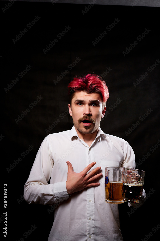 Young handsome guy with red hair in white shirt drinking beer. Funny man with emotions on the face and beer mug in hand and black background. Alcoholic is happy with alcohol