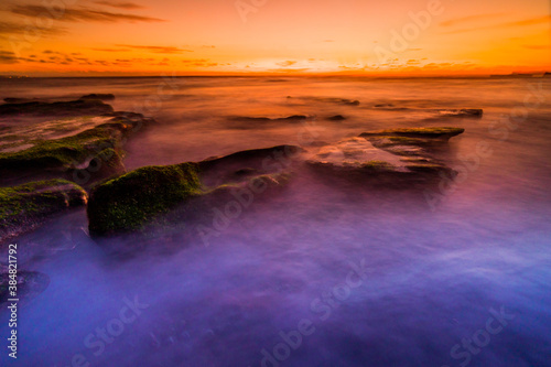 A beautiful sunset with long exposure technique at Mengening Beach Canggu Bali. a layer of moss on the beach rock makes a dream beach feel. 
