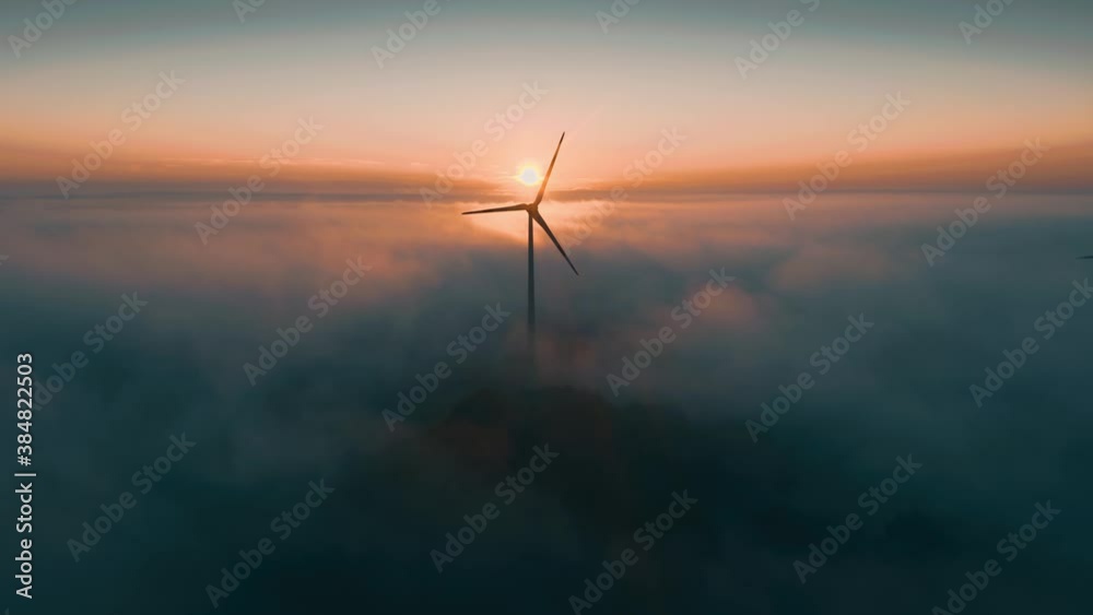 Wind turbine at sunrise in heavy fog. Wind farm generating green energy