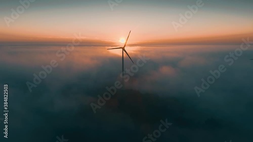 Wind turbine at sunrise in heavy fog. Wind farm generating green energy
