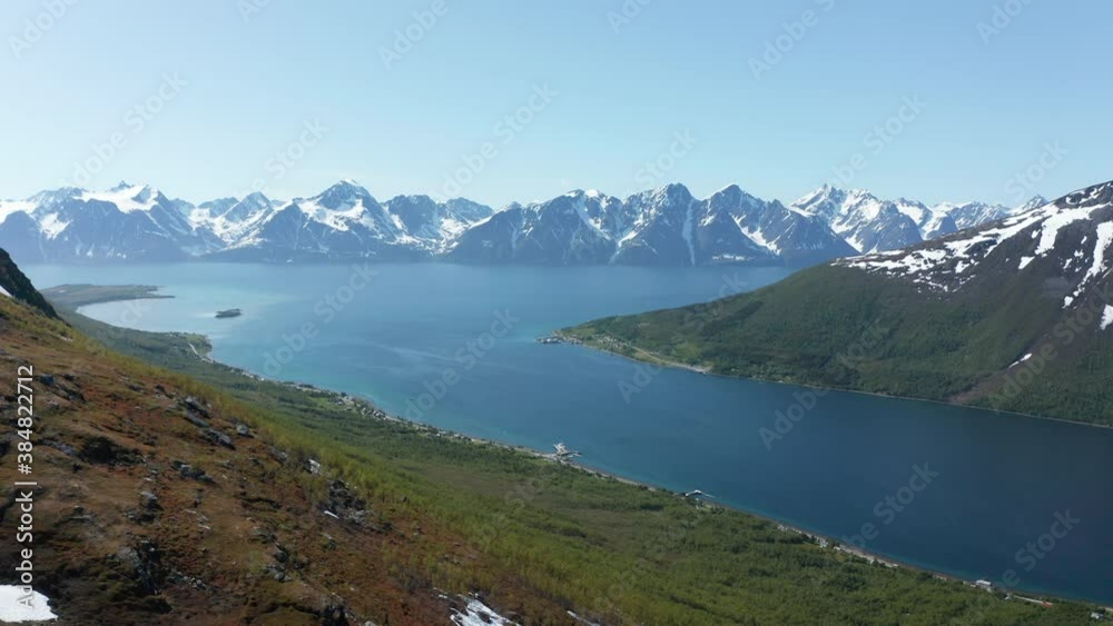 Aerial view overlooking the arctic ocean, snowy Lyngen mountains in the background, sunny, summer day, in Rotsund, Nordland, Norway - Descending, drone shot Aerial view overlooking the arctic ocean, snowy Lyngen mountains in the background, sunny, summer day, in Rotsund, Nordland, Norway - Descending, drone shot