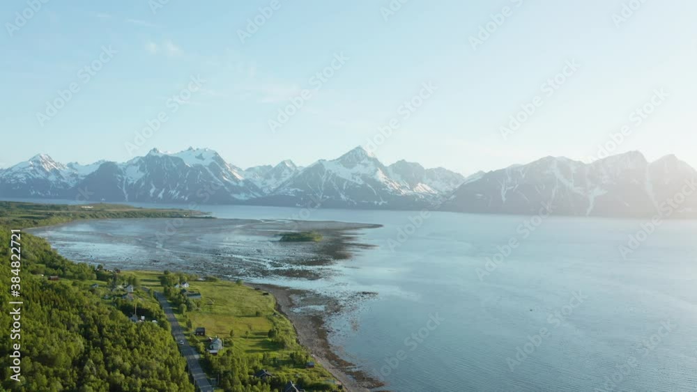 Aerial view over houses and a road, towards shallow sea at the Arctic ocean and snowy peak in the background, sunny, summer day, in Rotsund, Troms, Nordland, Norway - dolly, drone shot Aerial view over houses and a road, towards shallow sea at the Arctic ocean and snowy peak in the background, sunny, summer day, in Rotsund, Troms, Nordland, Norway - dolly, drone shot