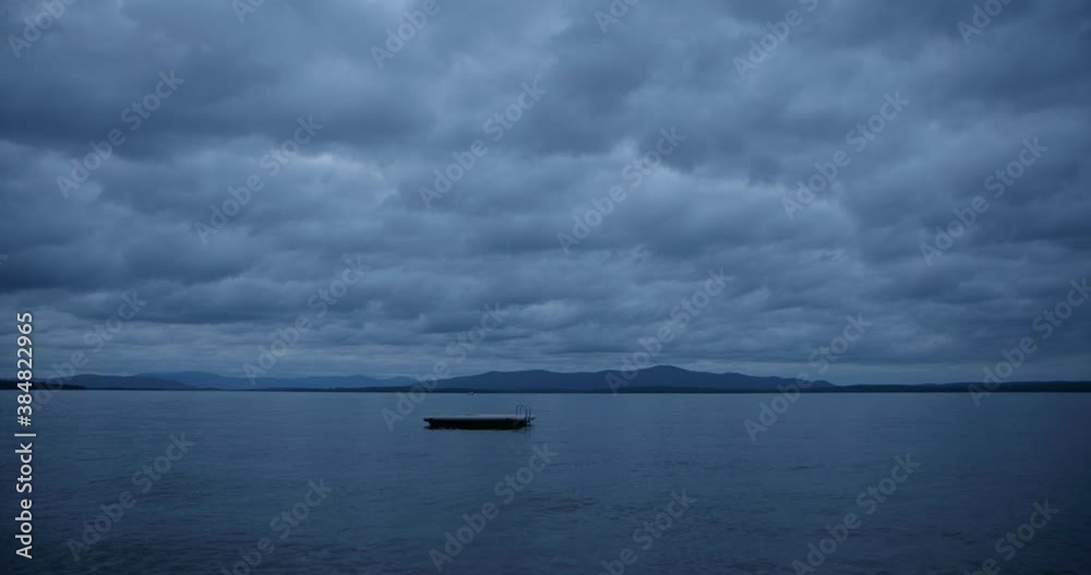 Wide shot small lonely boat sitting on calm waters under dramatic stormy sky