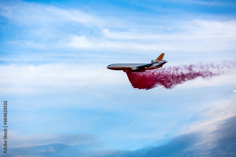 Fototapeta premium Emergency response tanker airplane drops fire retardant over a wildfire blue skies with clouds