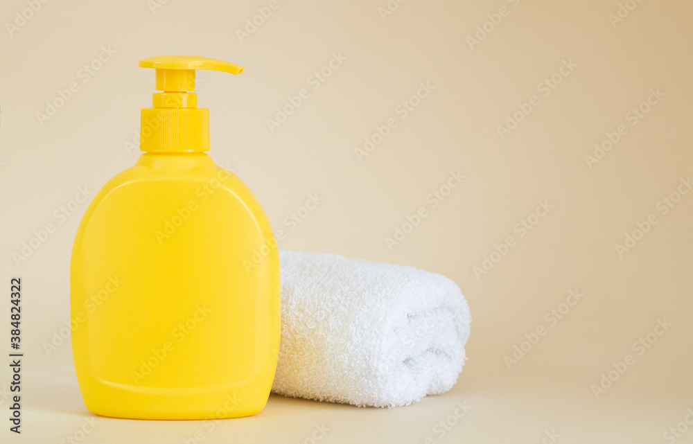 Yellow unbranded dispenser bottle next to white towel on beige background Yellow unbranded dispenser bottle next to white towel on beige background