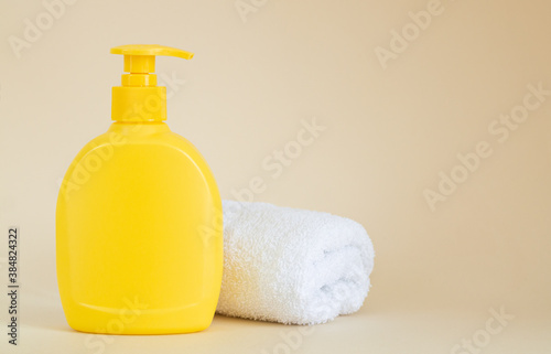 Yellow unbranded dispenser bottle next to white towel on beige background