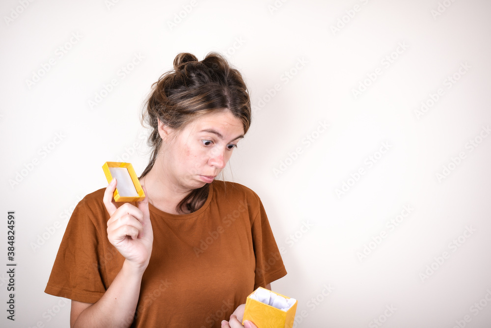 Upset woman wearing brown t-shirt holding empty gift box isolated over pink background