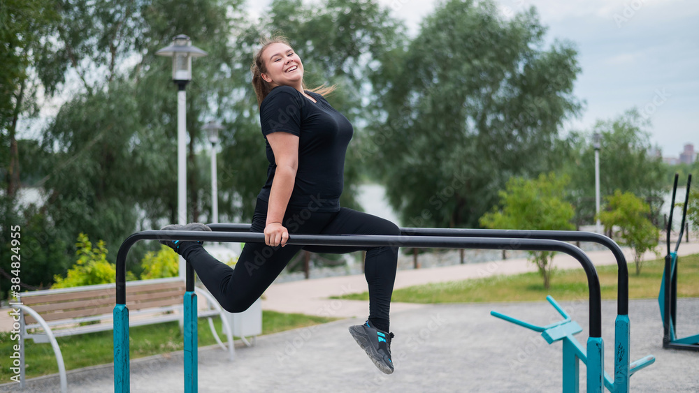 Plump young woman doing exercises on the uneven bars outdoors. Caucasian girl doing push-ups