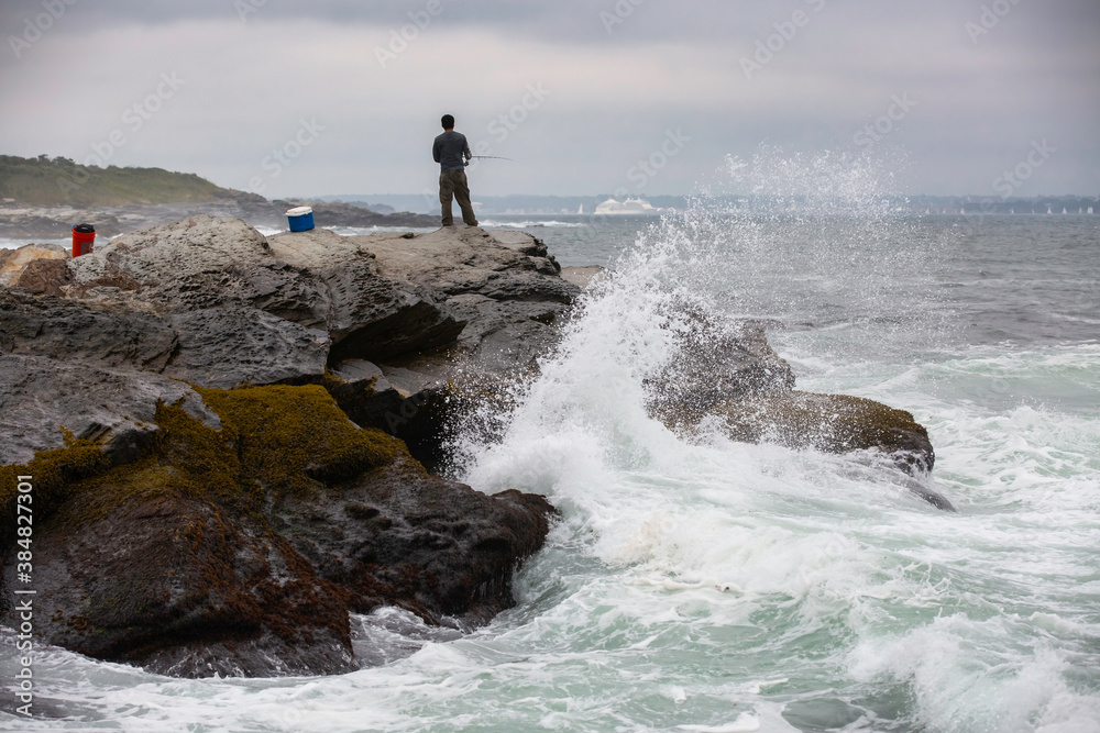 A fisherman with fishing equipment, fishing on top of dangerous rocky coastline with waves crashing in Beavertail State Park, Rhode Island A fisherman with fishing equipment, fishing on top of dangerous rocky coastline with waves crashing in Beavertail State Park, Rhode Island