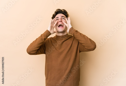 Young caucasian man isolated on beige background shouting excited to front. © Asier