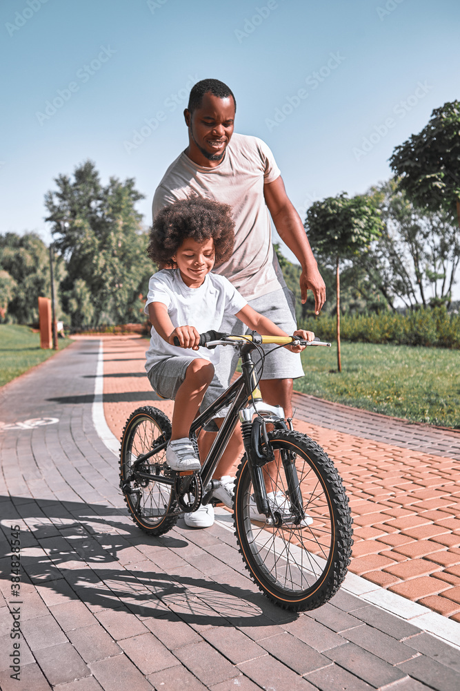 Caring father supporting his kid in learning how to cycle Caring father supporting his kid in learning how to cycle