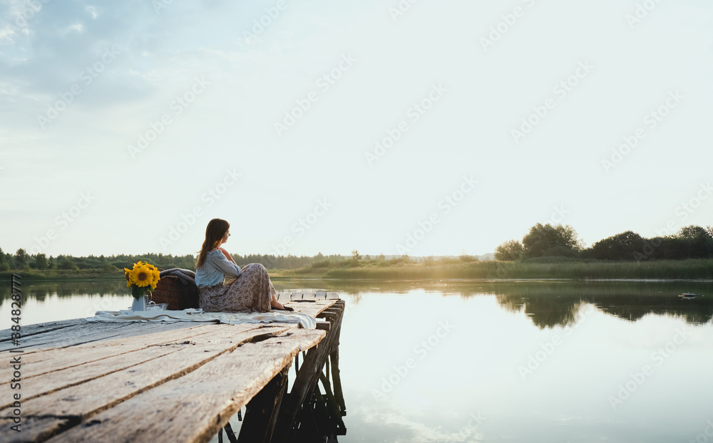 Young Girl sits on a Wooden Pier on the Lake and Enjoy the View of the Sunrise, River, Forest