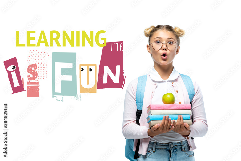 Shocked schoolgirl holding apple and books near learning is fun lettering on white Shocked schoolgirl holding apple and books near learning is fun lettering on white
