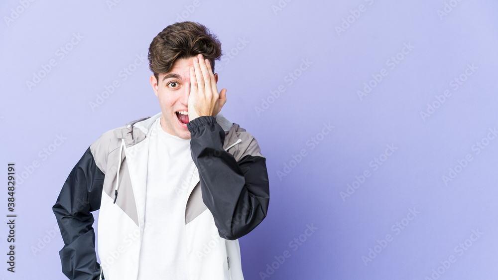 Young caucasian man isolated on purple background having fun covering half of face with palm. Young caucasian man isolated on purple background having fun covering half of face with palm.