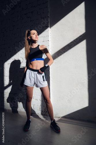 A pretty long-haired brunette of athletic build stands against a brick wall in the loft