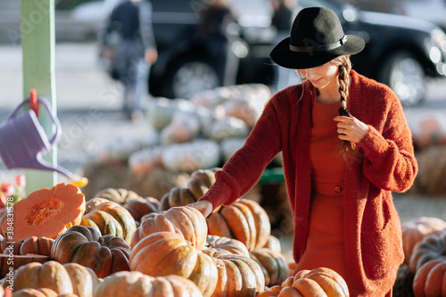 Portrait of happy woman choosing ripe orange pumpkin on farmers market in brown sweater, dress. Cozy autumn vibes Halloween, Thanksgiving day