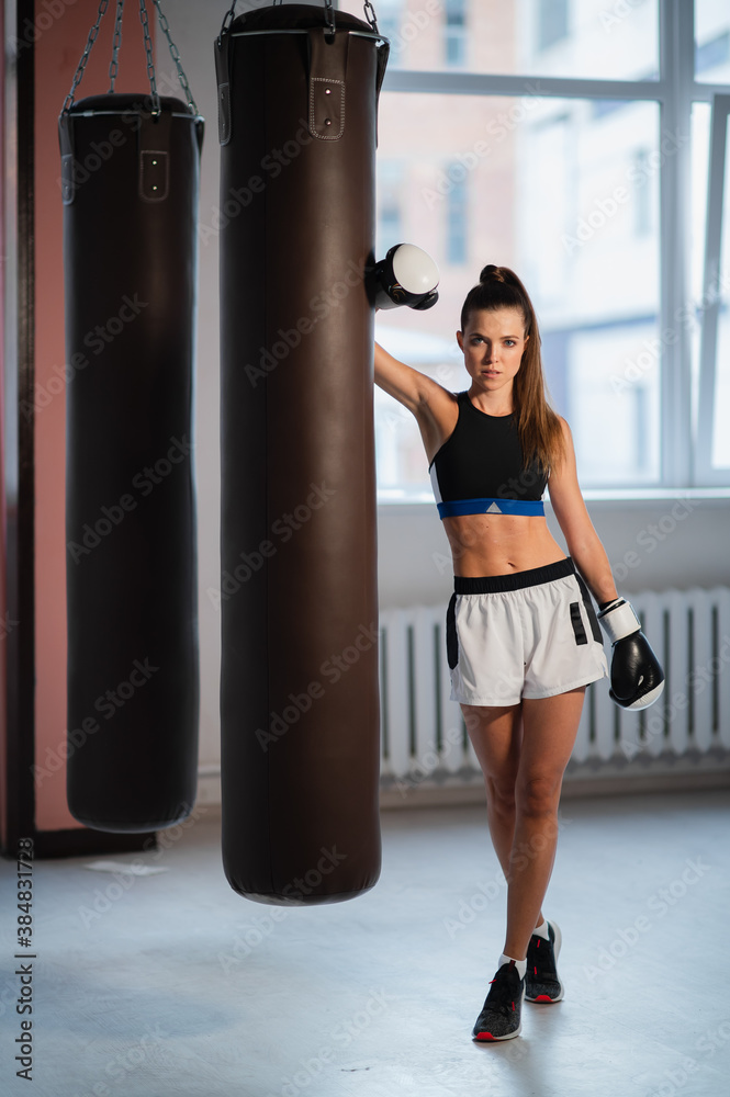 Cute girl posing for a photo in boxing gloves on the background of punching bags