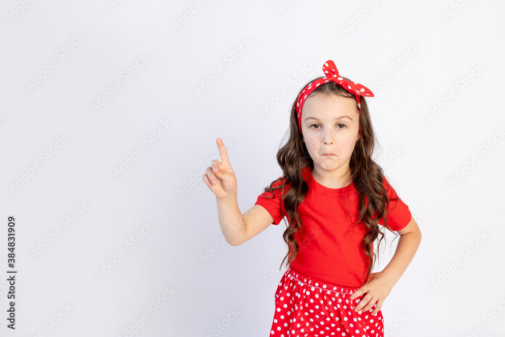 A cute little girl in a red outfit on a white isolated background shows a thumbs up. Space for text.the concept of the celebration and sales A cute little girl in a red outfit on a white isolated background shows a thumbs up. Space for text.the concept of the celebration and sales