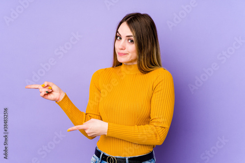 Young caucasian woman isolated on purple background shocked pointing with index fingers to a copy space.