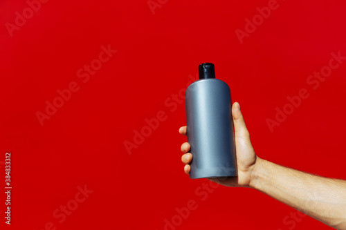 Man holding a grey bottle isolated on red background.Man hand holding a bottle (on red background)