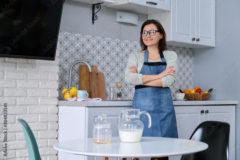 Home portrait of mature woman housewife in apron in kitchen Home portrait of mature woman housewife in apron in kitchen