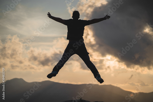 Hiker jumps and enjoys a stunning sunset from the peak of a mountain