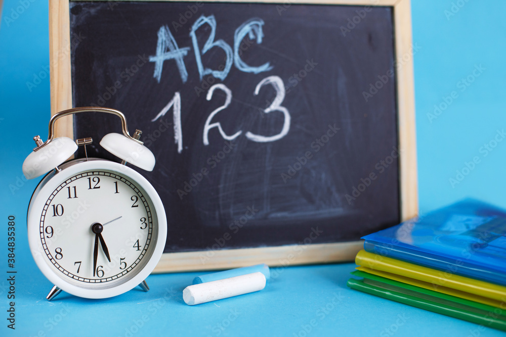 Textbooks and alarm clock with school chalkboard on a blue background. Back to school. Concept Education or business Textbooks and alarm clock with school chalkboard on a blue background. Back to school. Concept Education or business