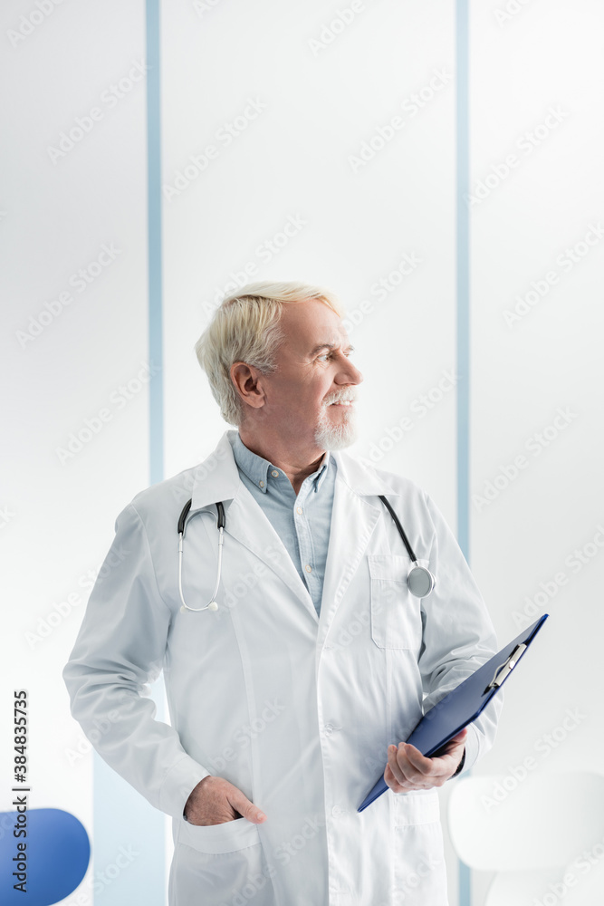 Grey haired doctor in white coat holding clipboard in hospital Grey haired doctor in white coat holding clipboard in hospital