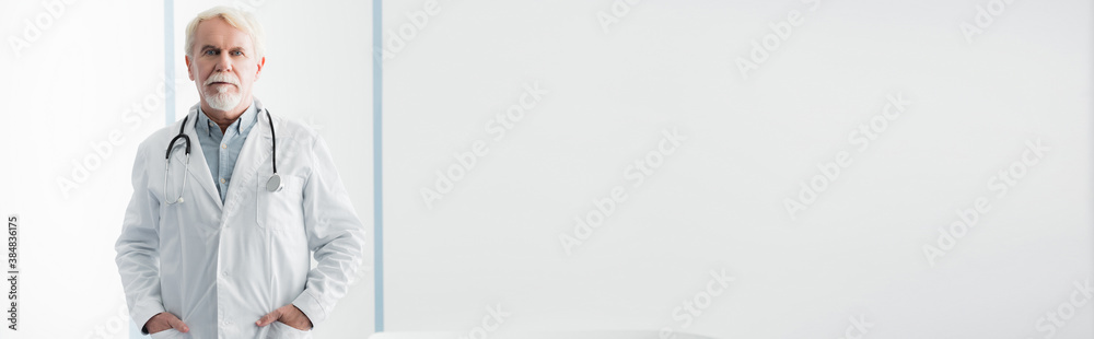 Panoramic crop of grey haired doctor looking at camera in clinic Panoramic crop of grey haired doctor looking at camera in clinic