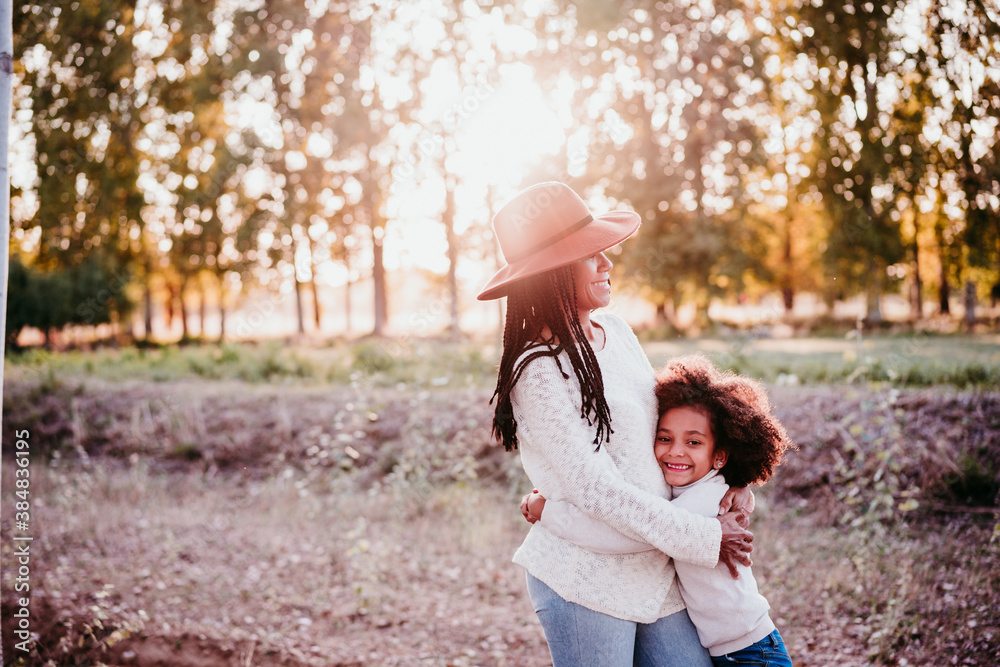 Fototapeta premium portrait of hispanic mother and afro kid girl outdoors at sunset during golden hour. Autumn season. Family concept