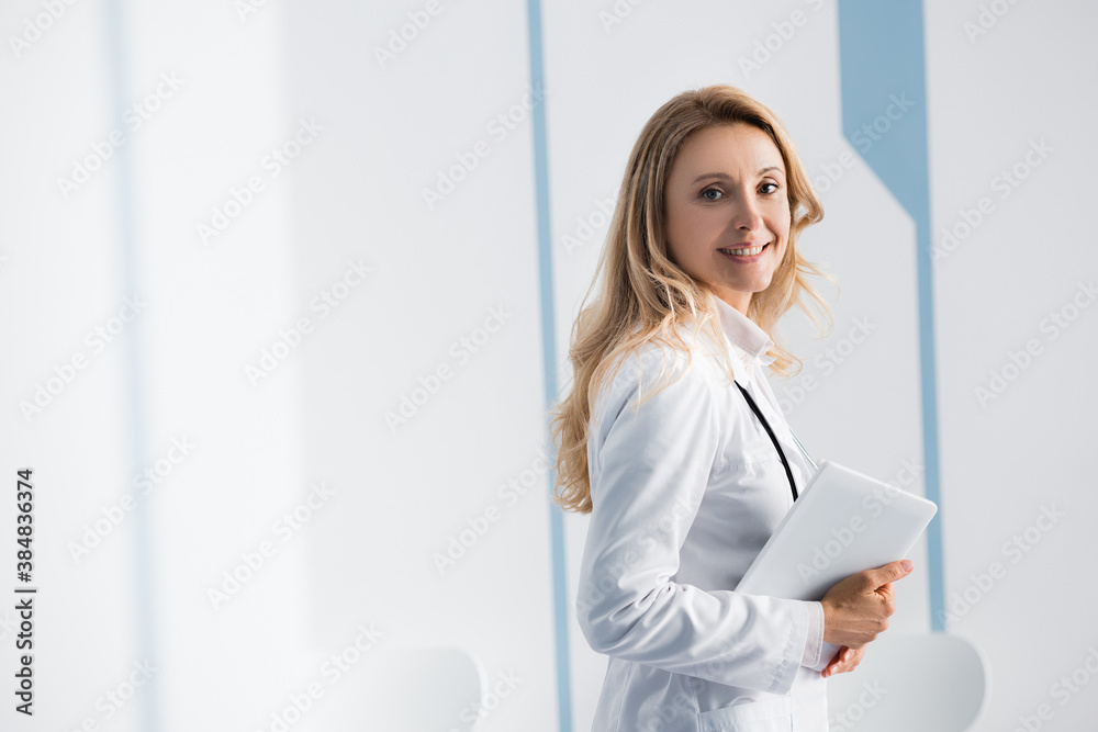 Selective focus of blonde doctor with digital tablet looking at camera in hospital Selective focus of blonde doctor with digital tablet looking at camera in hospital